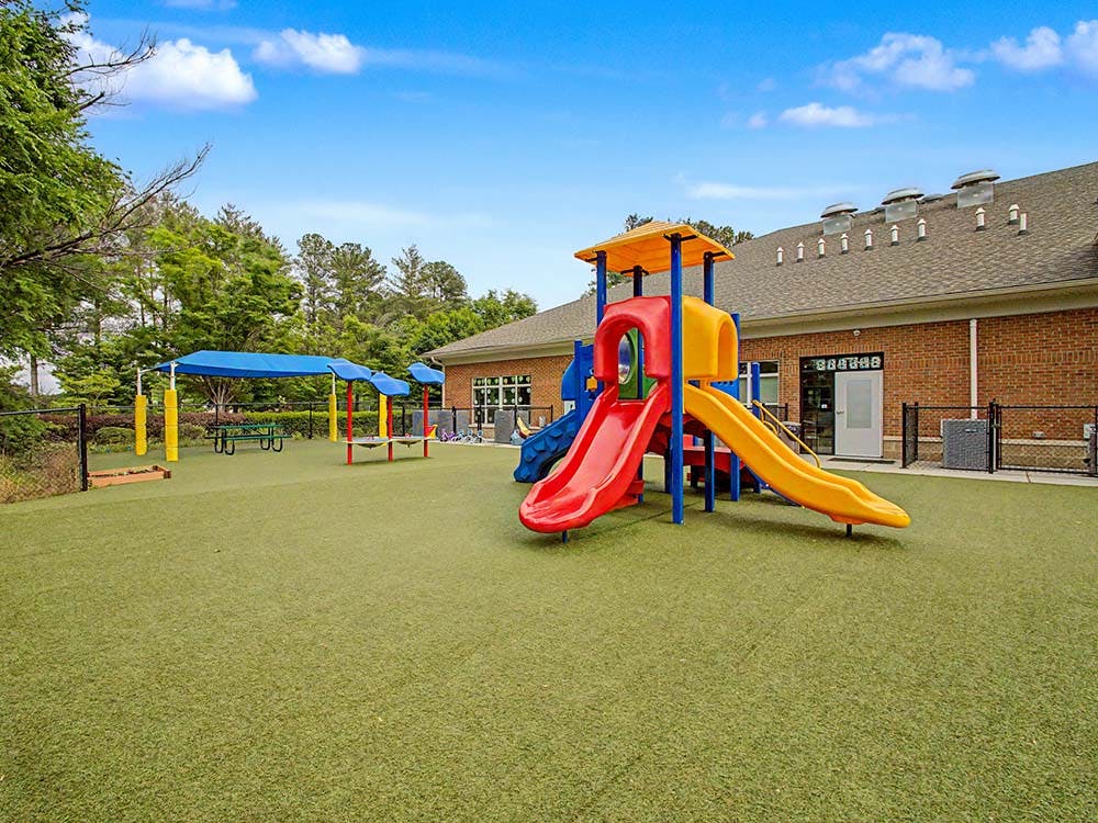Colorful playground with slides on artificial turf next to a brick building