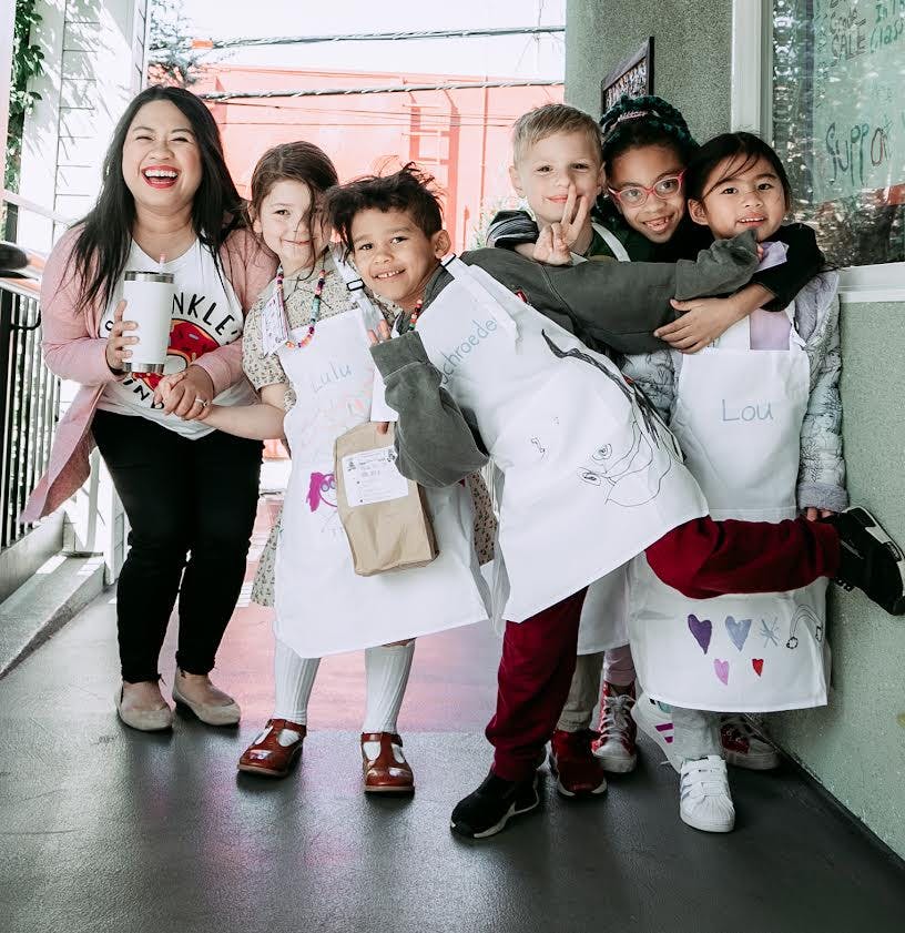 Adult and multiple children posing together, some wearing aprons