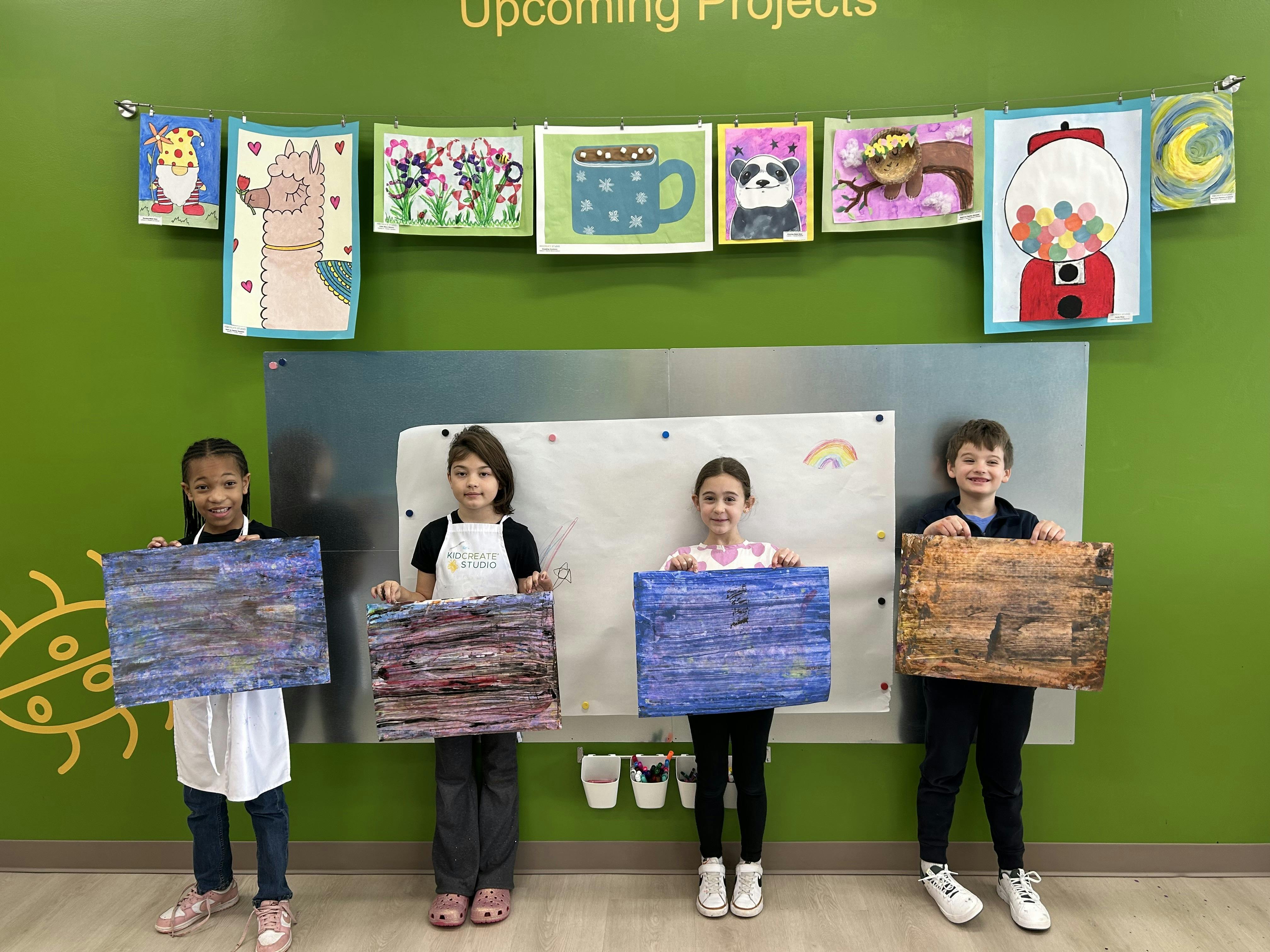 Four children holding up their abstract painted canvases in a classroom