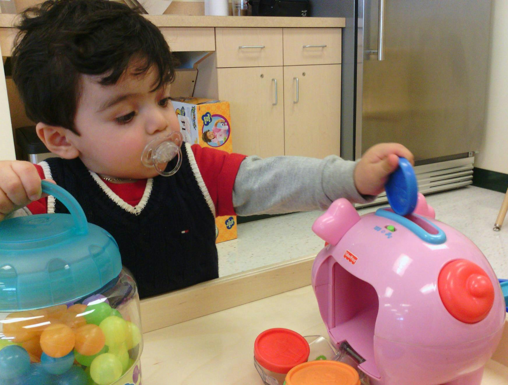 Child with pacifier playing with a toy piggy bank