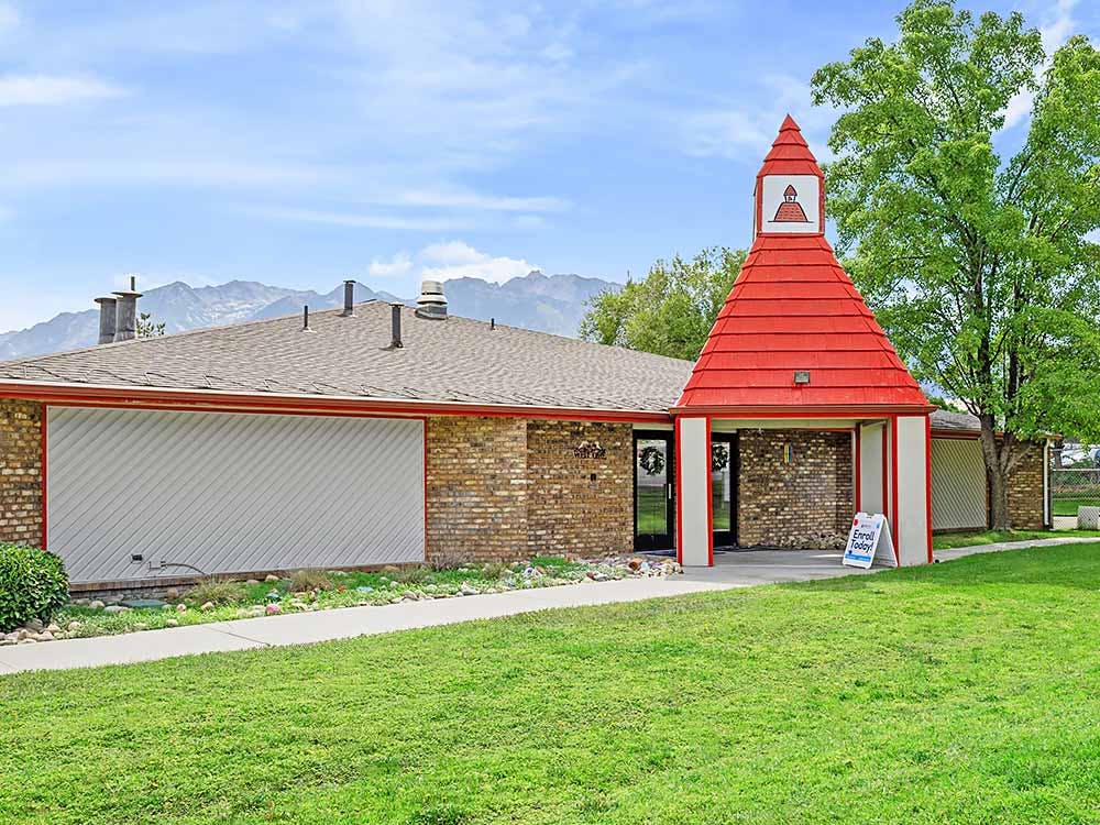 Brick building with a red pointed roof entry against a mountain backdrop