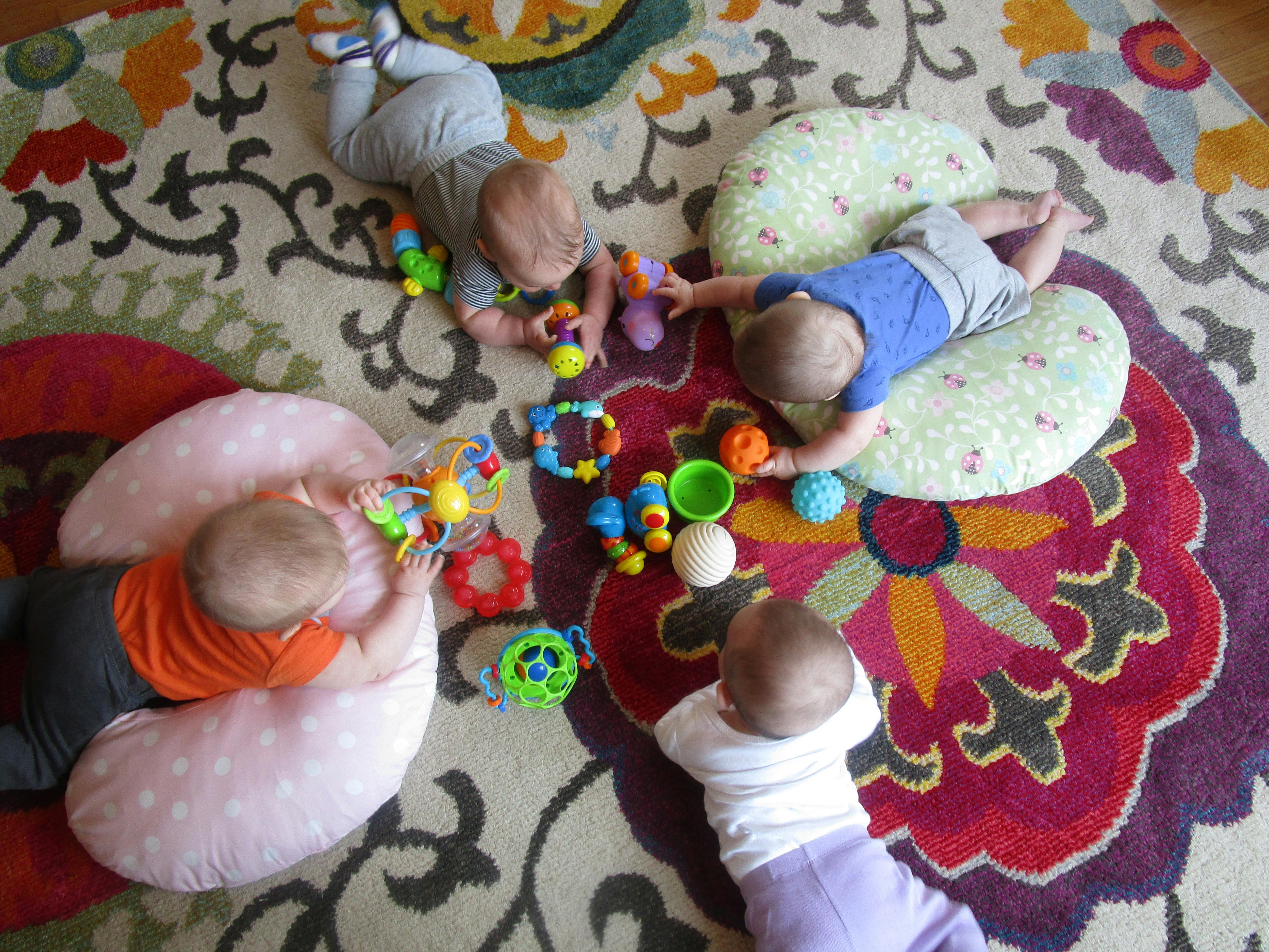 Multiple babies playing with toys on a patterned rug