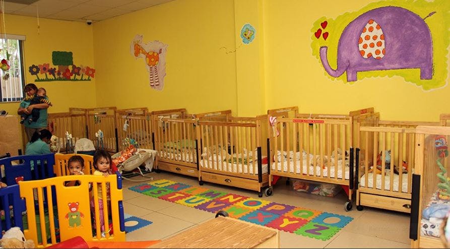 People and children in a room with multiple cribs and playpens