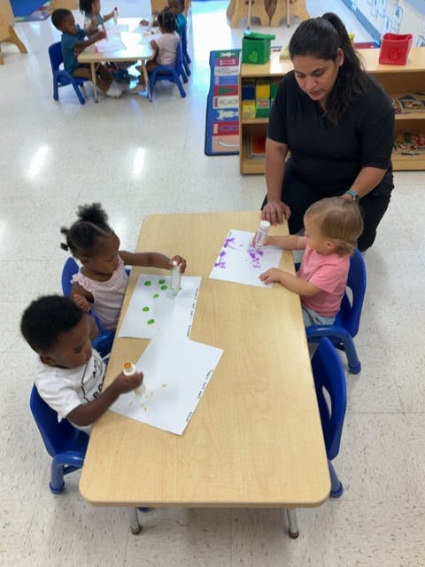 Adult and three children doing crafts at a table in a classroom