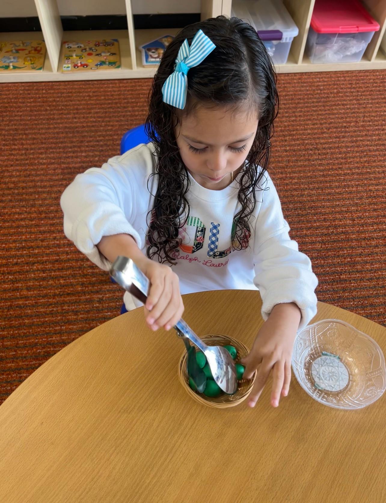 Child using a metal scoop to move small green objects between containers