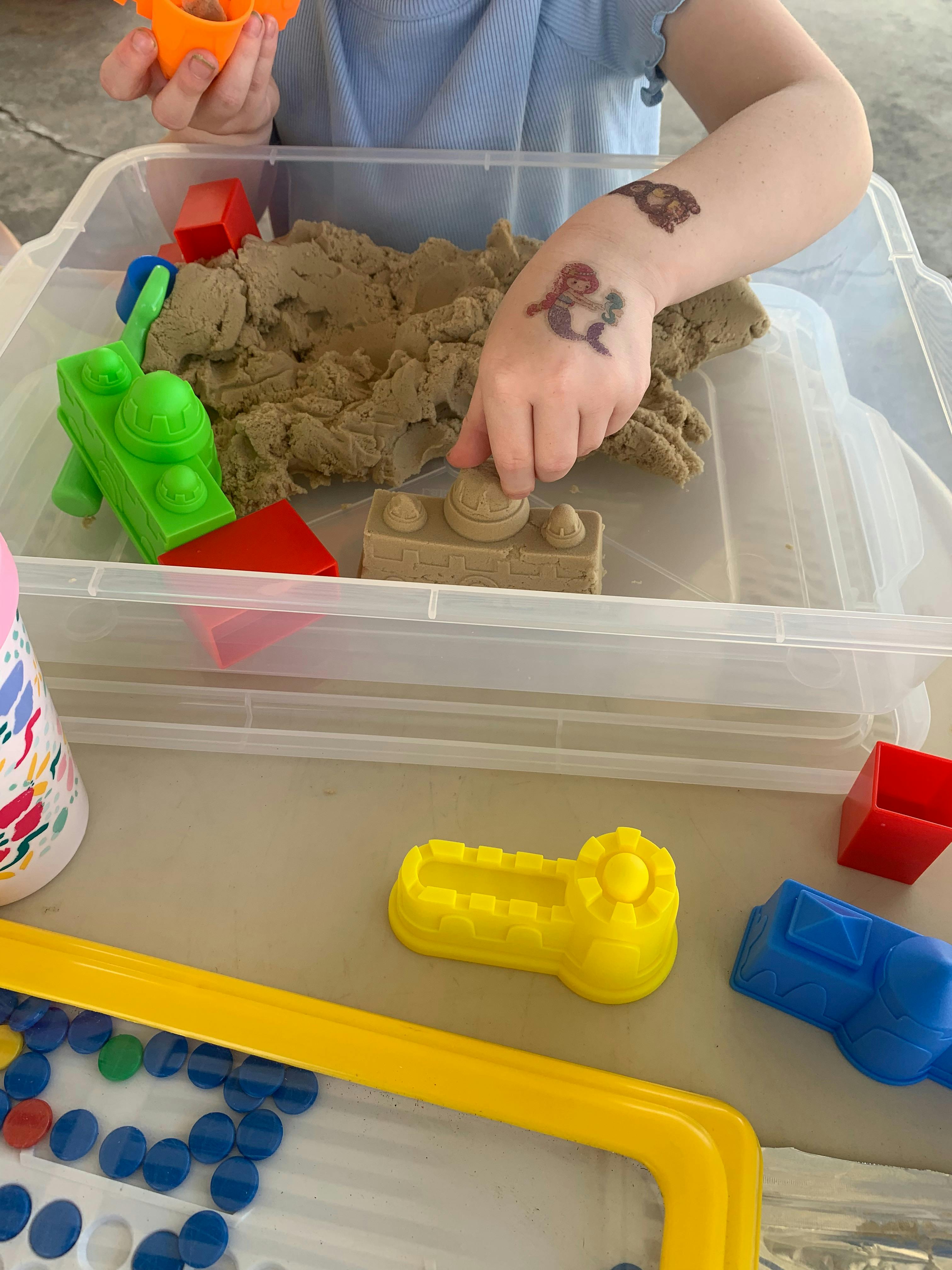 Child playing with kinetic sand and toys in a clear plastic bin