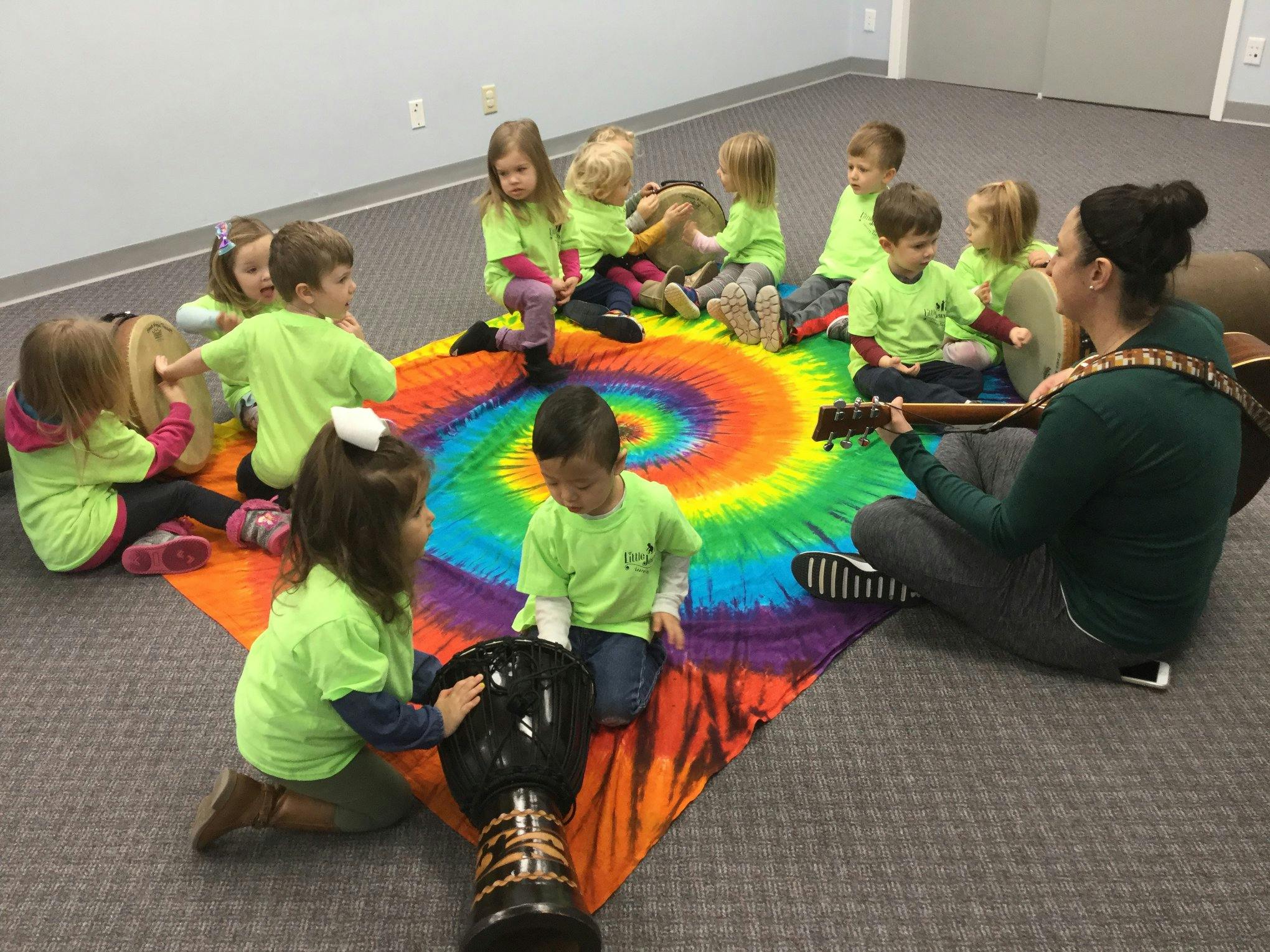 Person playing guitar for children sitting on a colorful mat