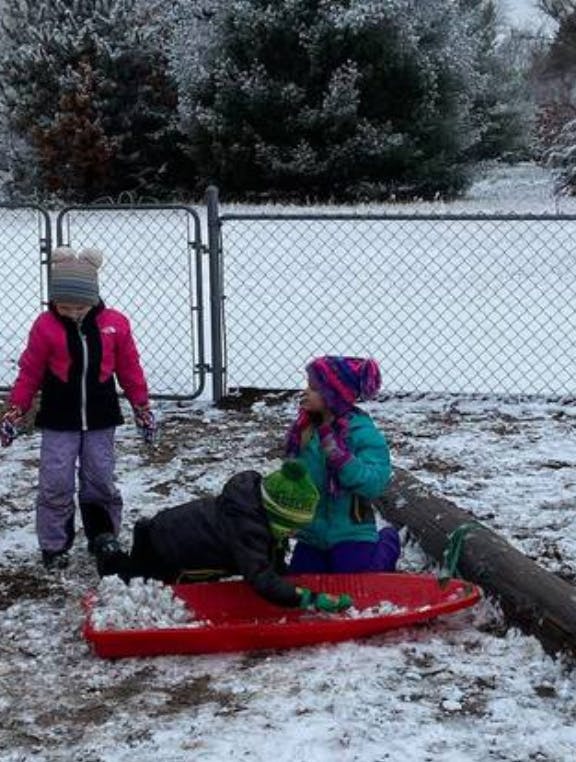 Three children playing in the snow with a red sled