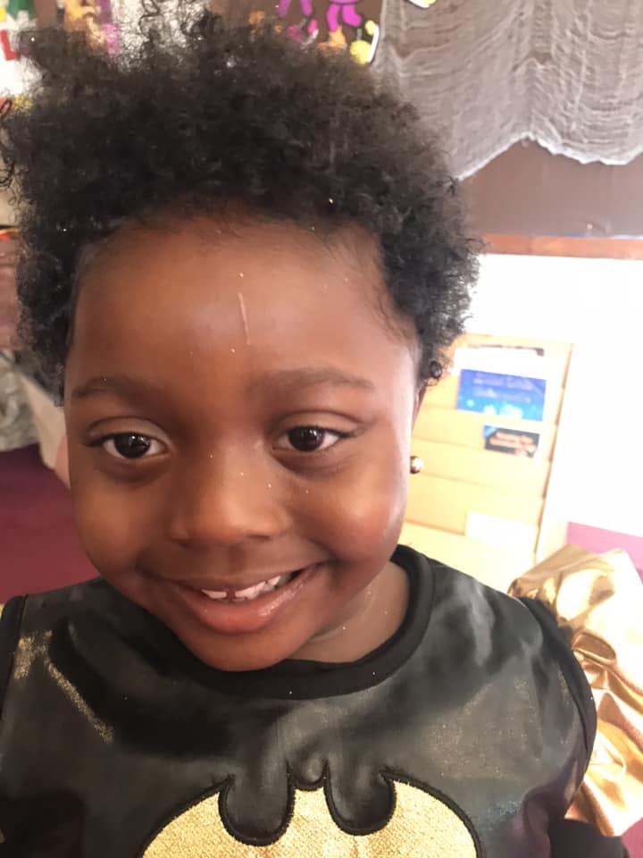 Child smiling in a black shirt with a gold Batman logo
