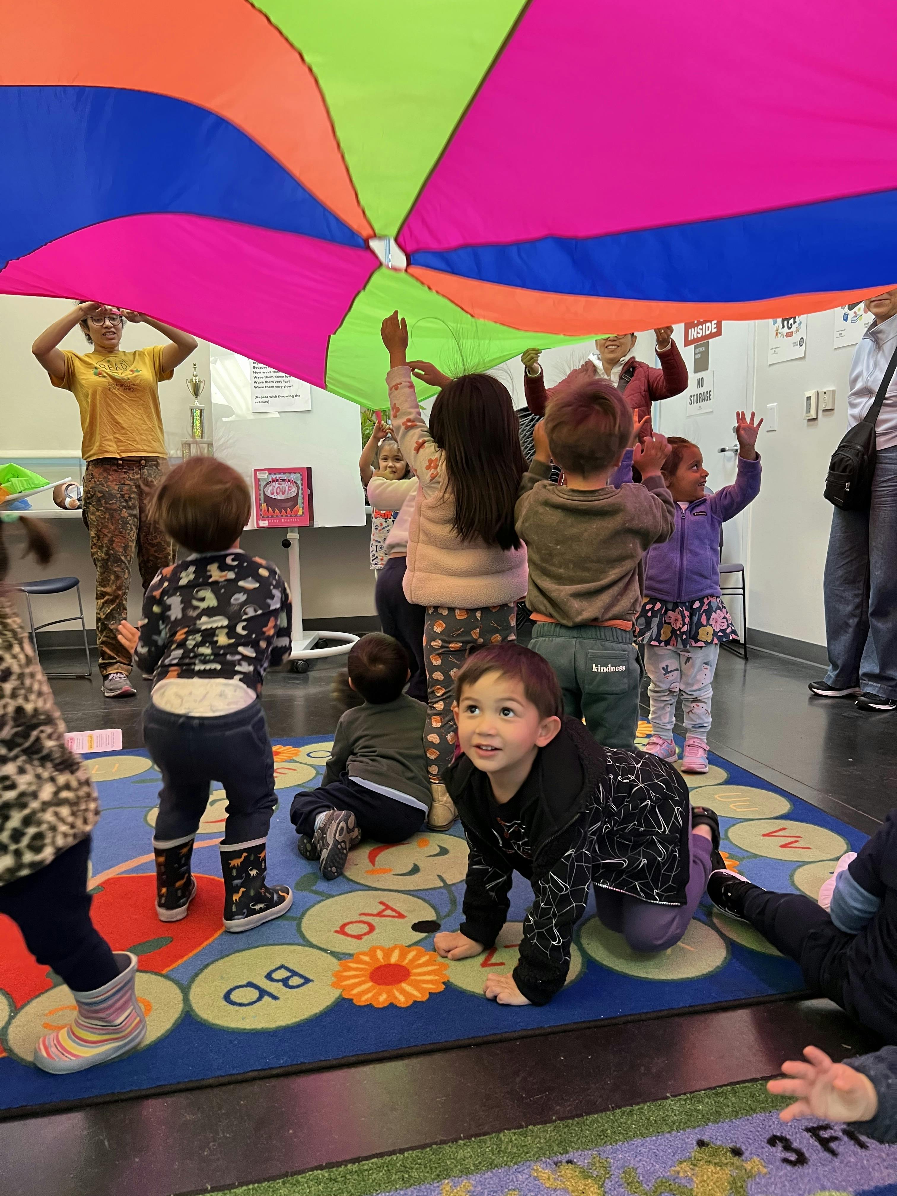 Adults and children playing with a large colorful parachute indoors