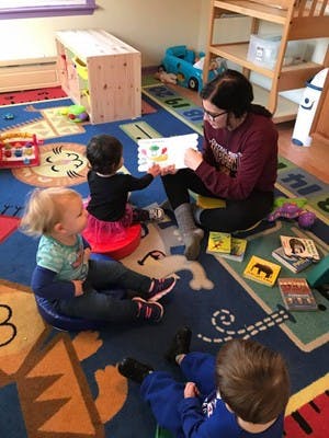 Person reading a book to three children in a classroom
