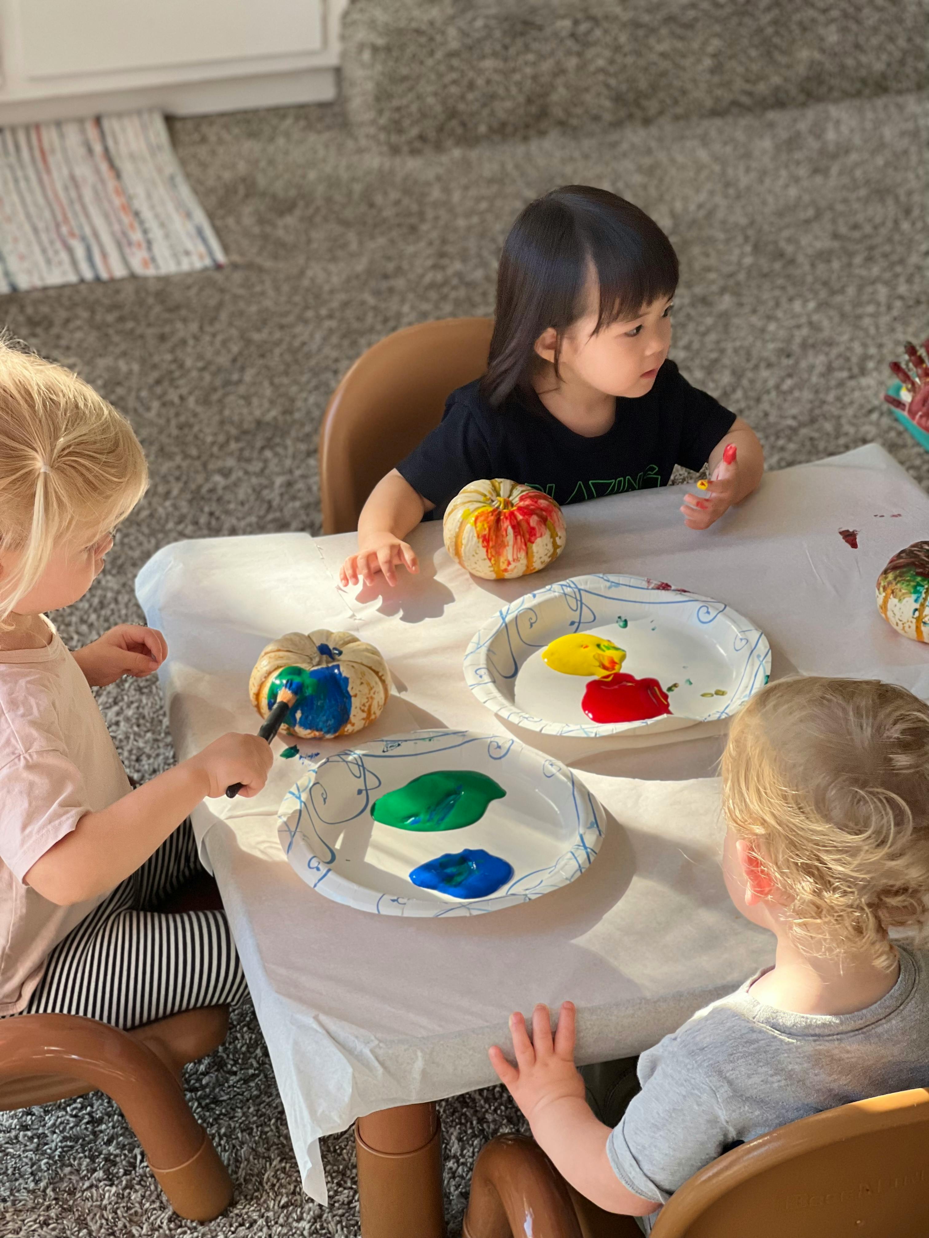 Three children painting small pumpkins at a table