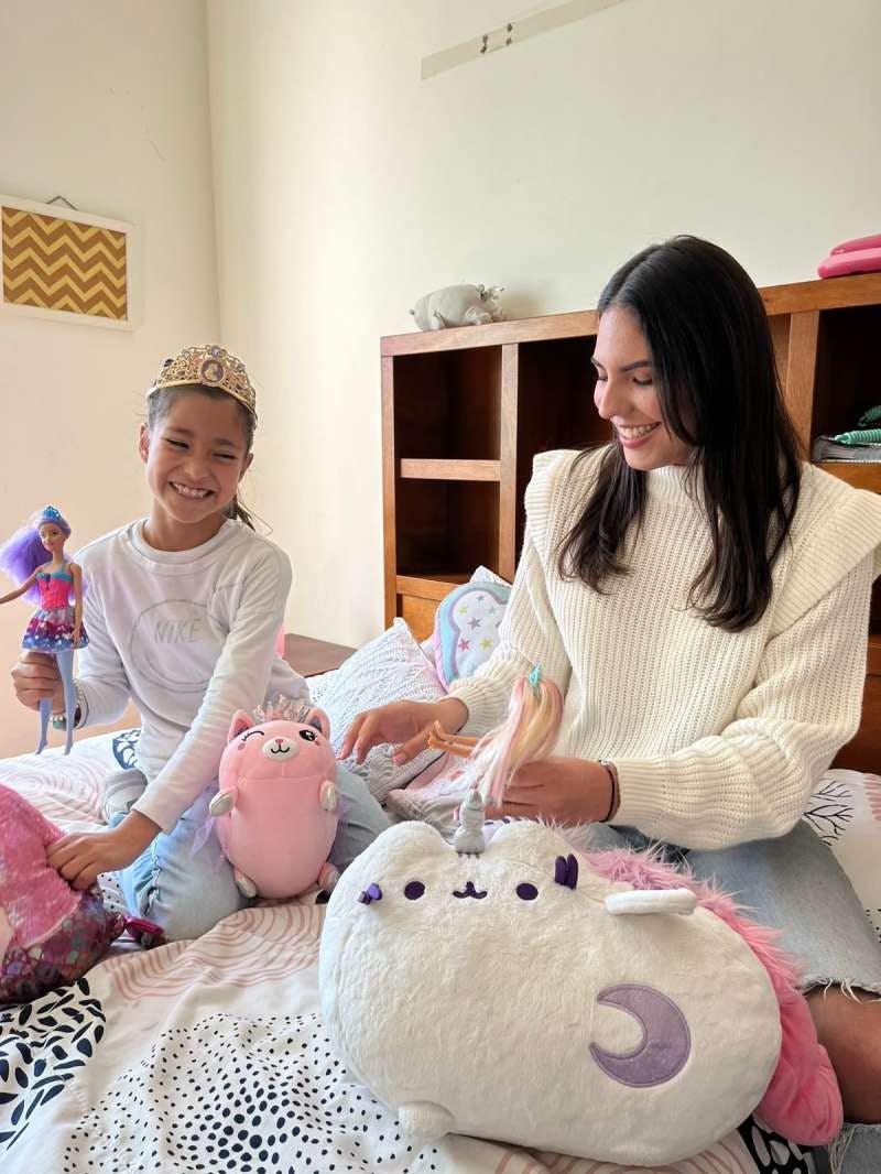 Two people playing with dolls and stuffed animals on a bed