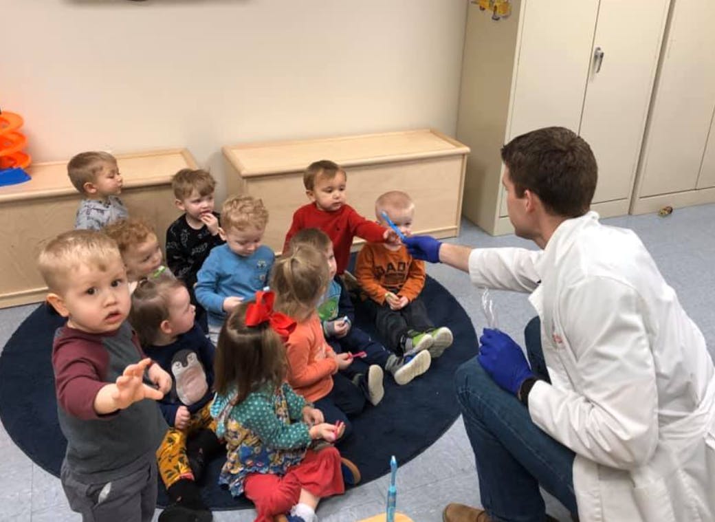 Person in lab coat interacting with a group of children