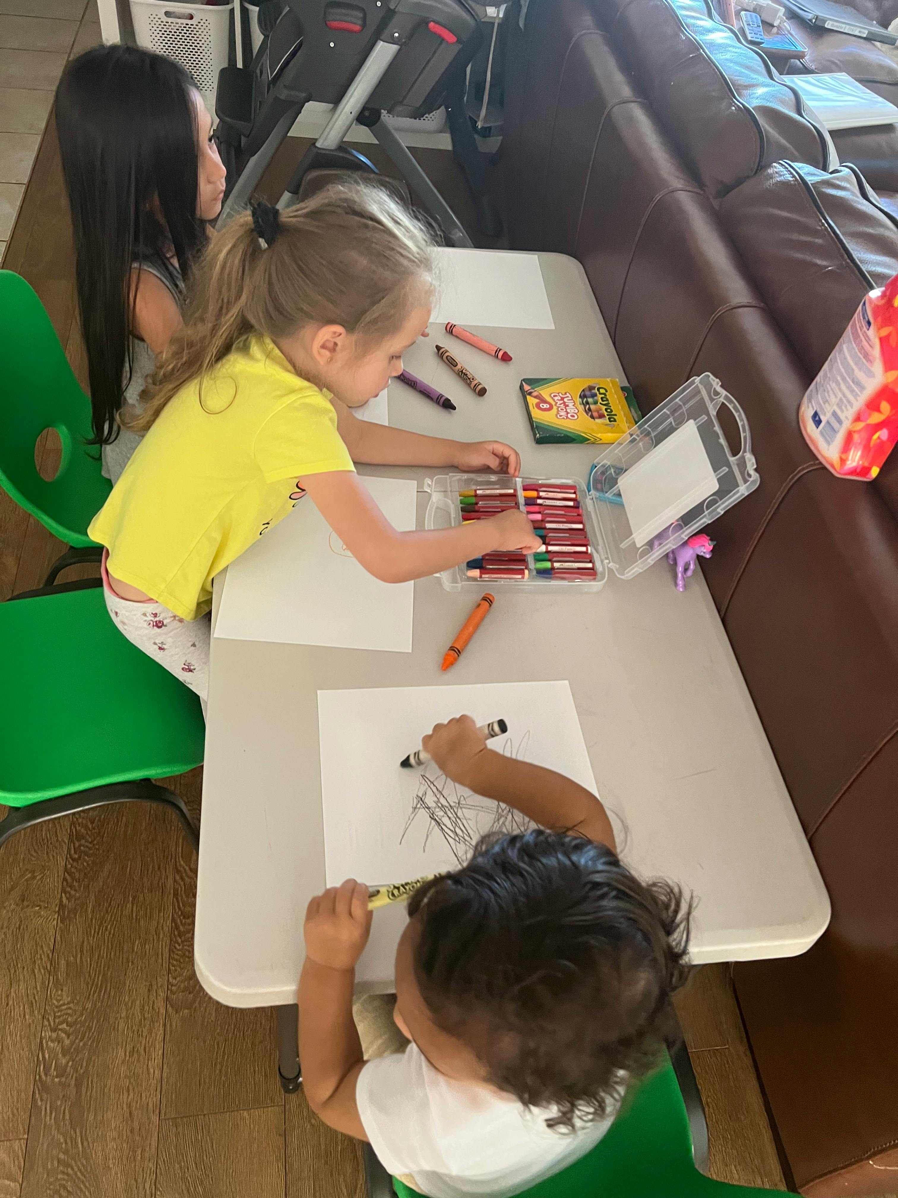 Three children drawing with crayons at a table