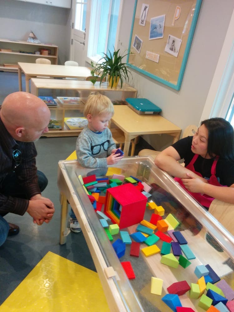 Adults watching a child play with colorful blocks in a classroom