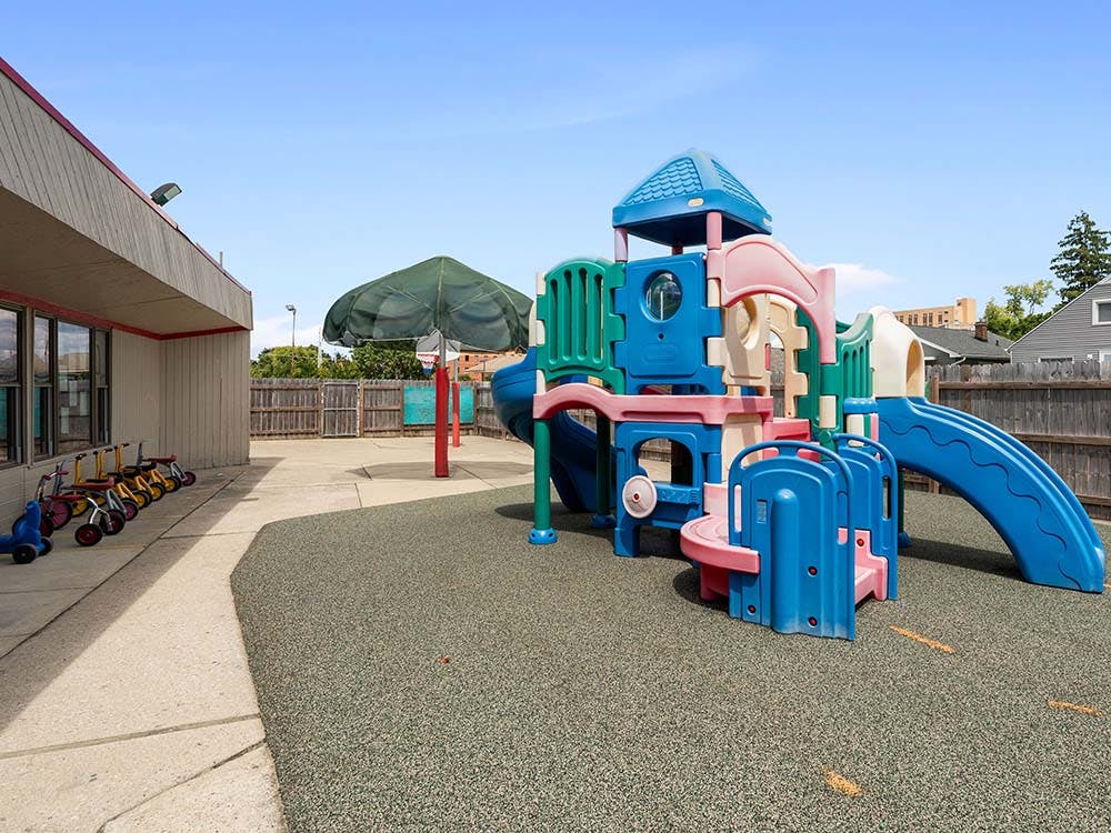 Colorful playground structure on rubber surfacing next to a building and tricycles