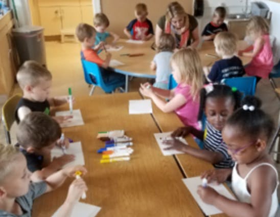 Children and adults sitting at tables, drawing and coloring