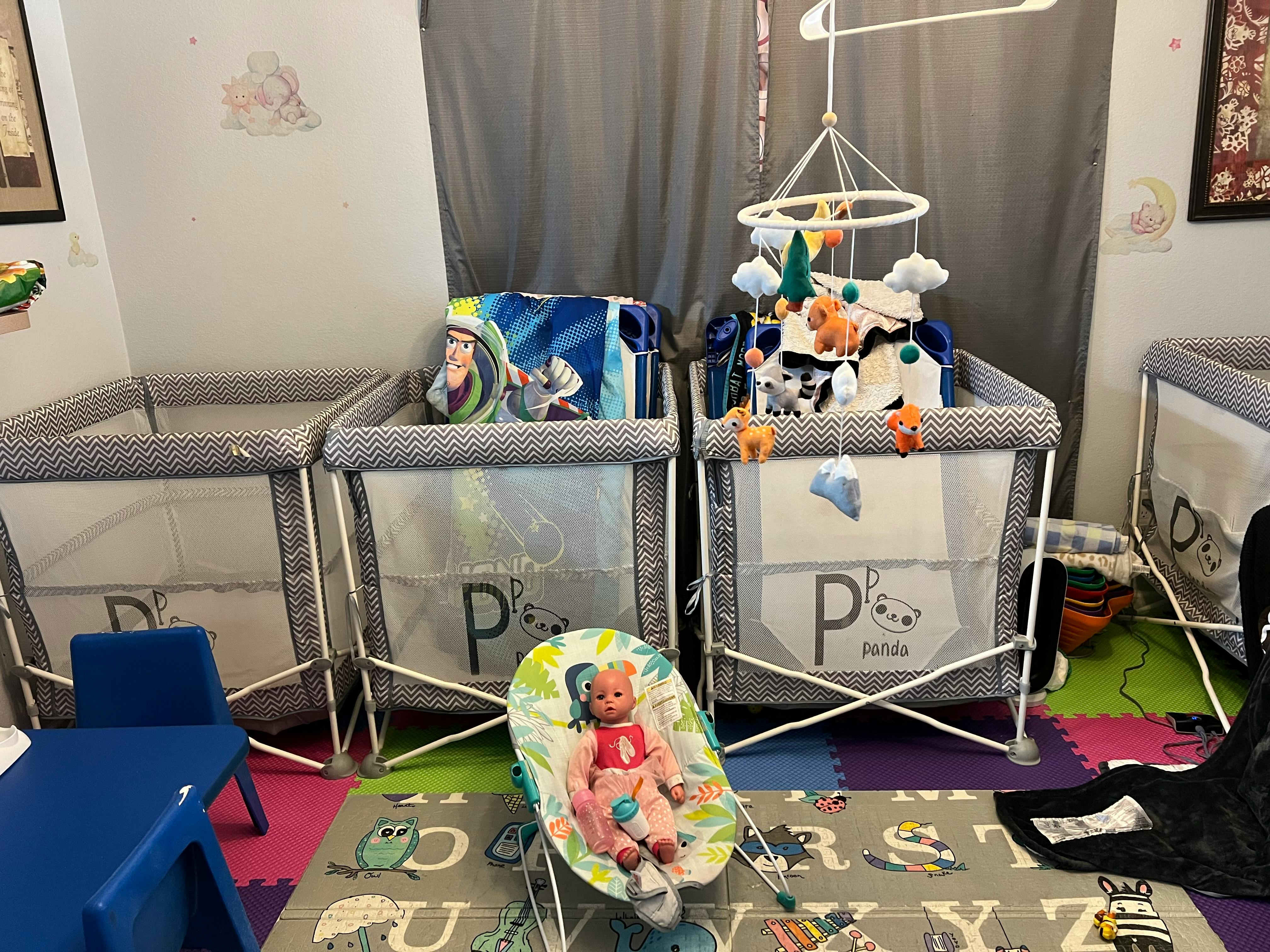 Multiple playpens with a baby bouncer and doll on a colorful mat