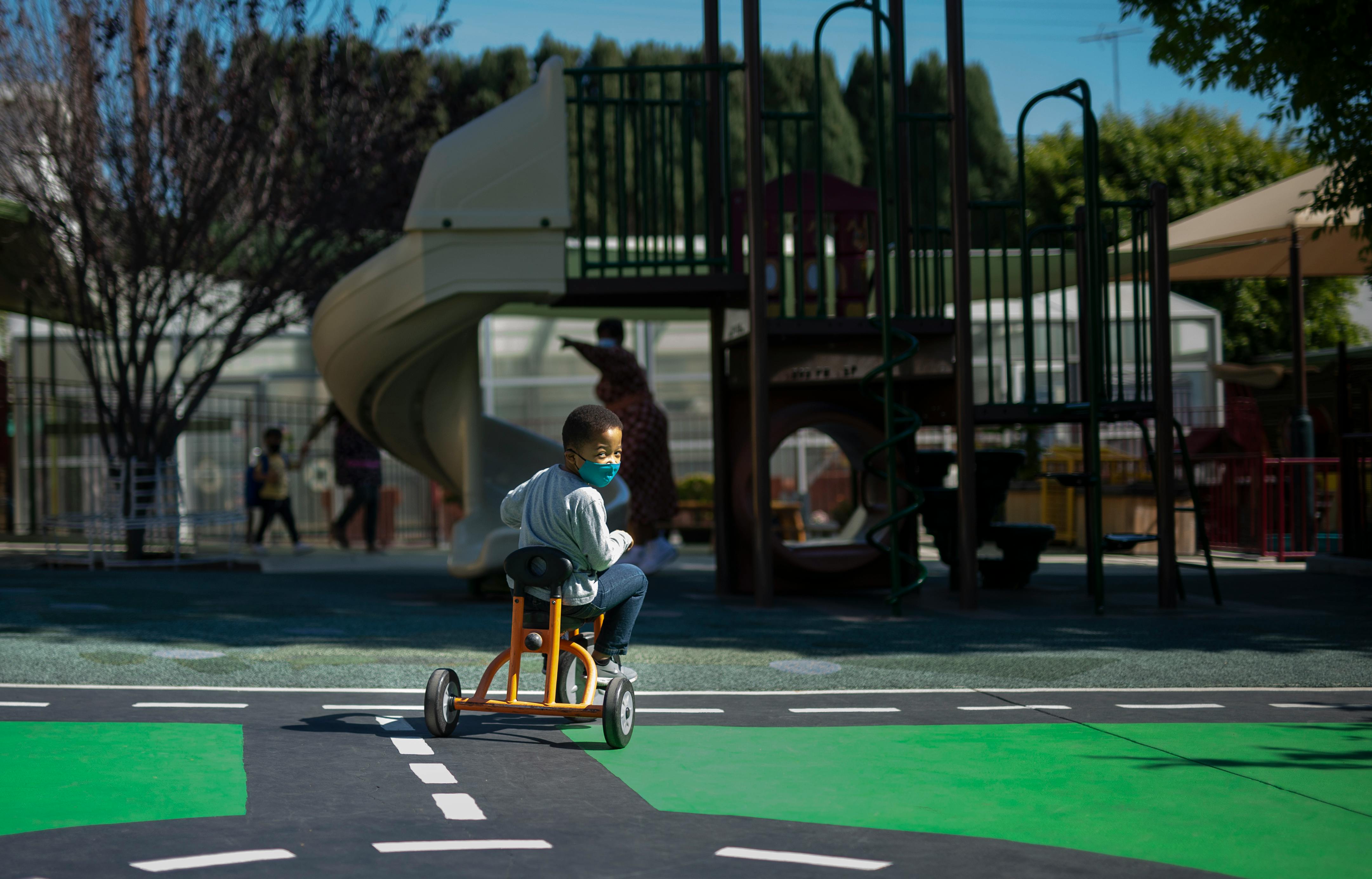 Child wearing a face mask riding a tricycle on a painted road in a playground