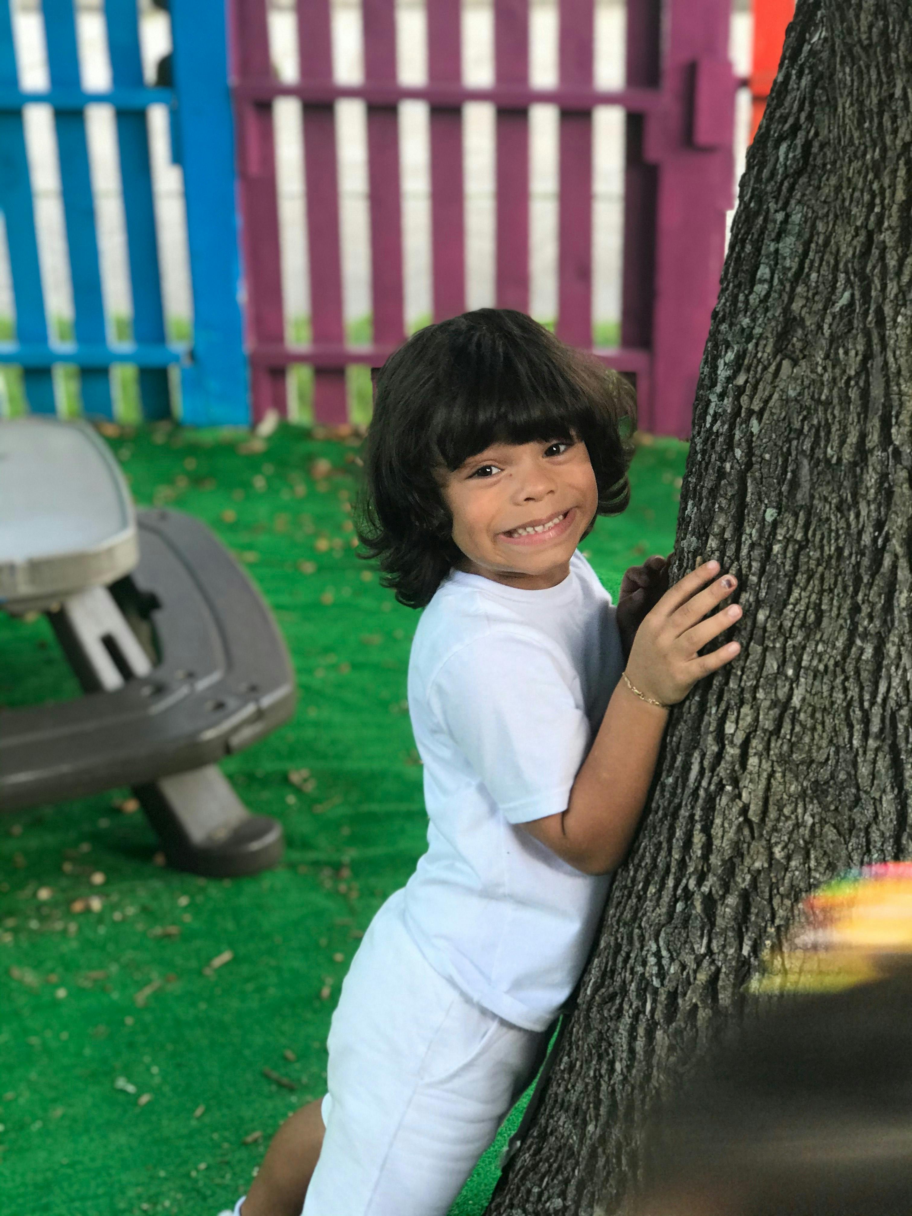 Child with dark hair leaning against a tree trunk