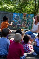 Adult reading a large book to a group of children outdoors