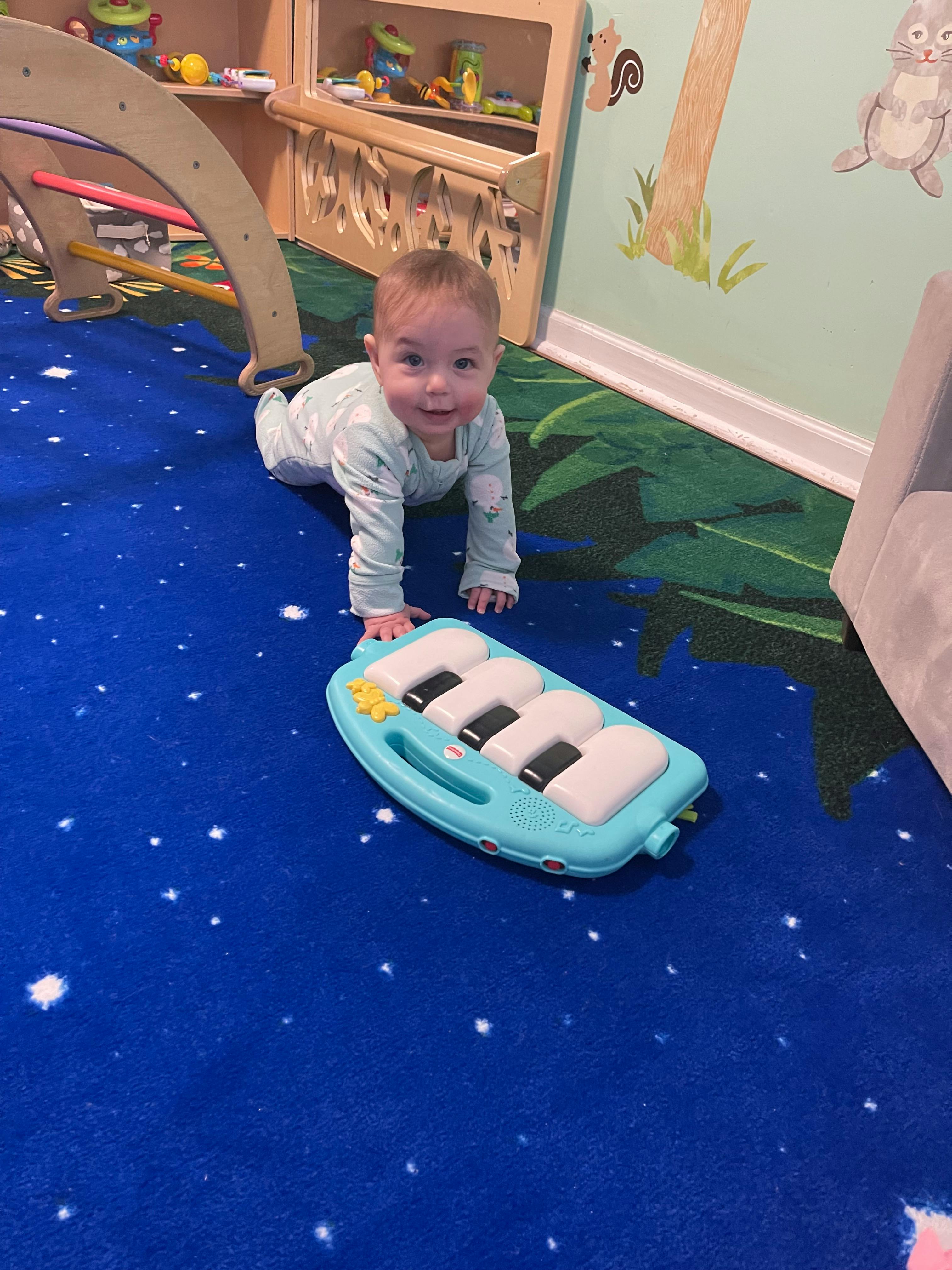 Child crawling on a blue carpet next to a toy piano