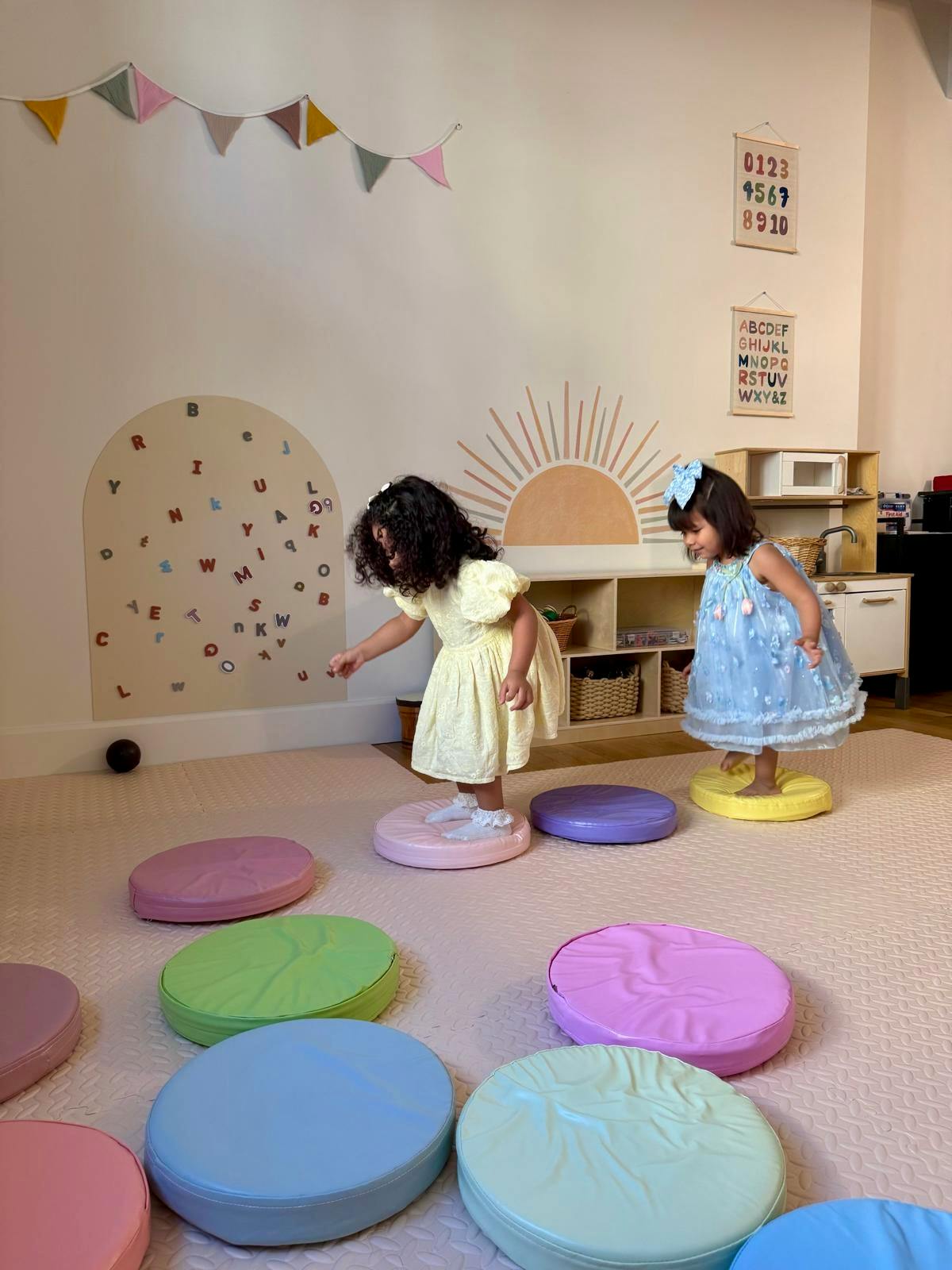 Two children stepping on round floor cushions in a playroom