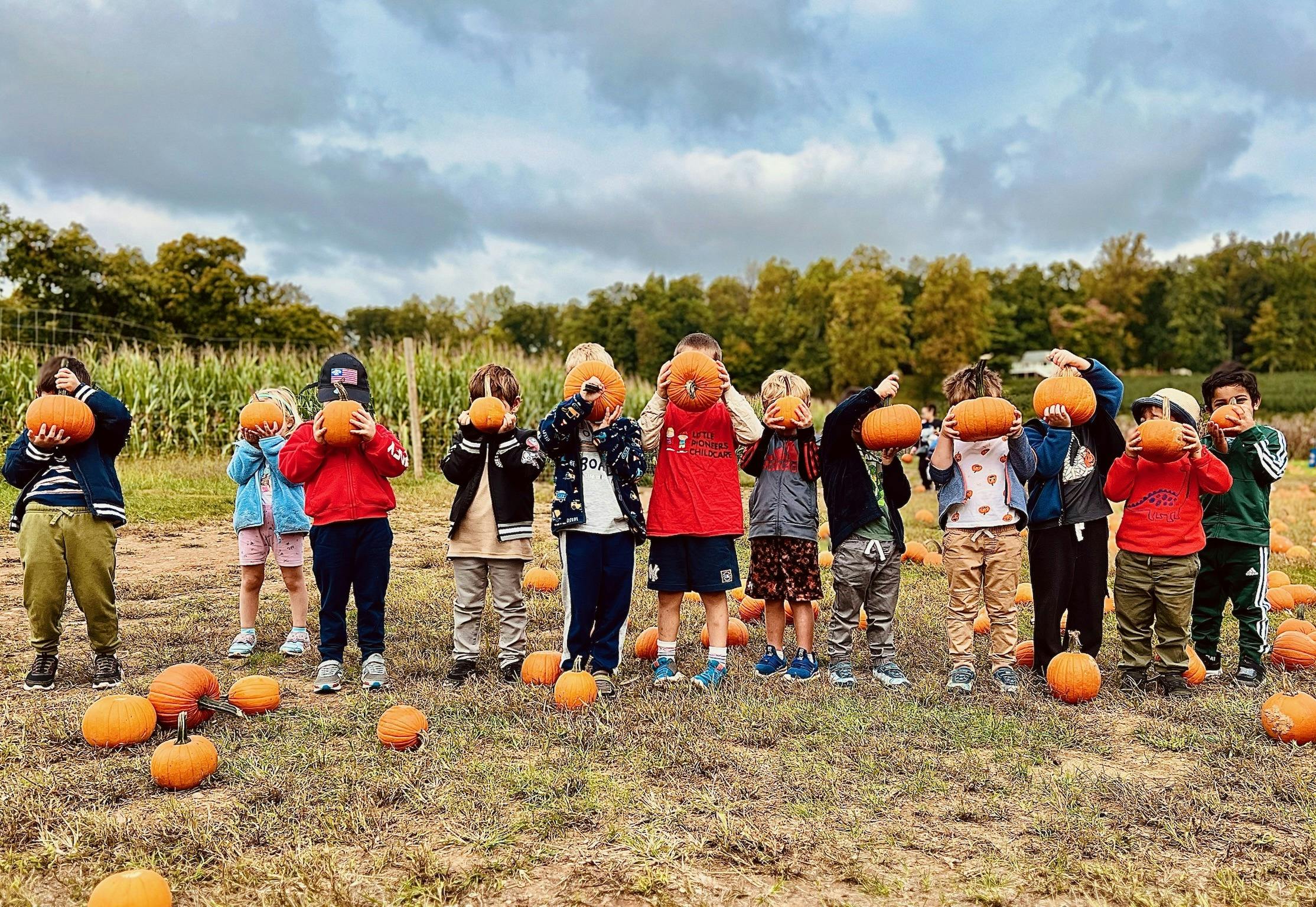 Group of children holding pumpkins in front of their faces in a field