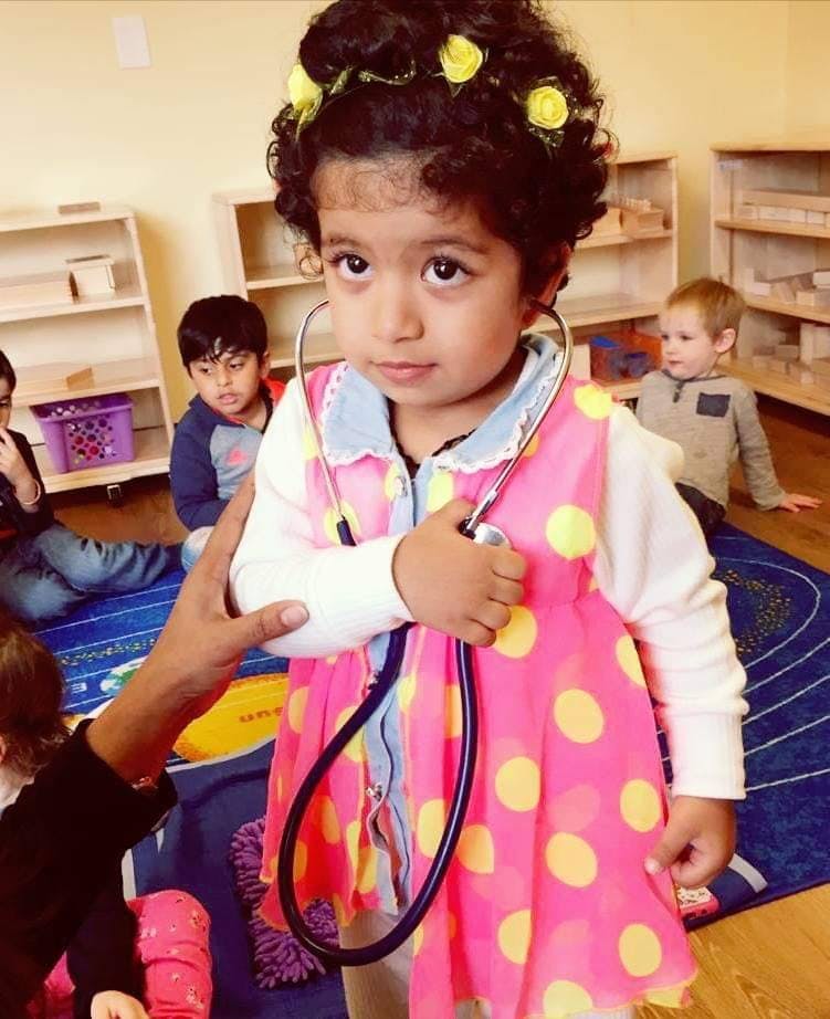 Child in a pink polka dot dress holding a stethoscope in a classroom