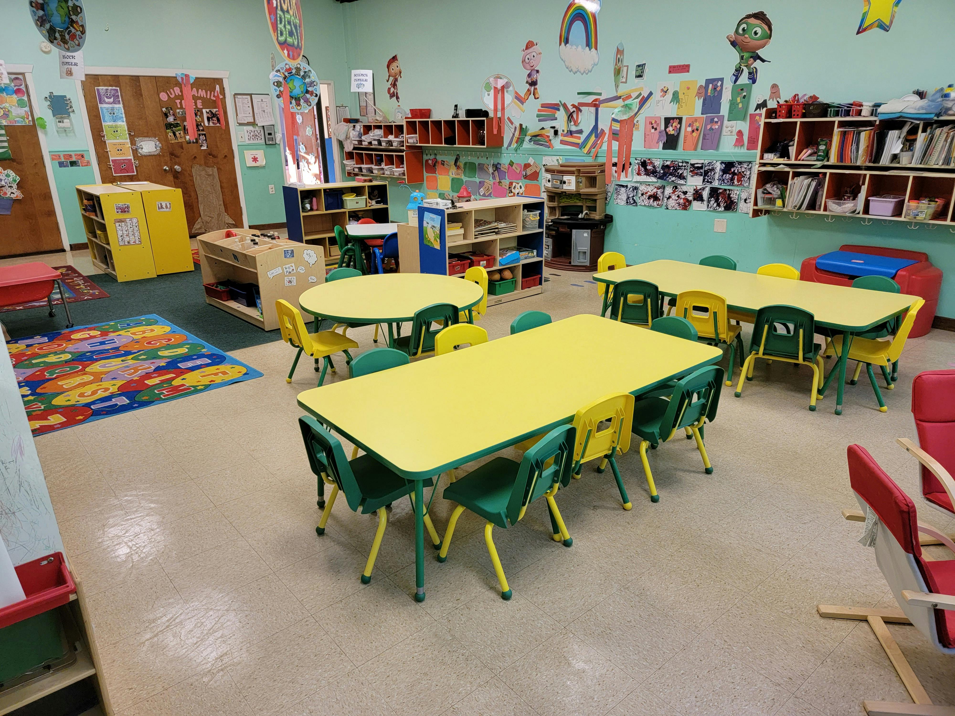 An empty colorful classroom with yellow tables and green chairs