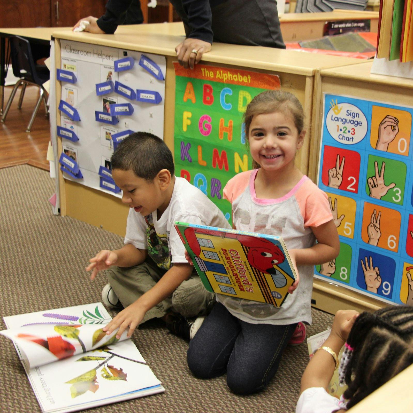 Two children sitting on the floor with books in a classroom