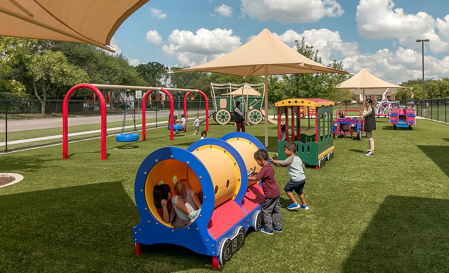 Children playing on a train-shaped tunnel and other playground equipment