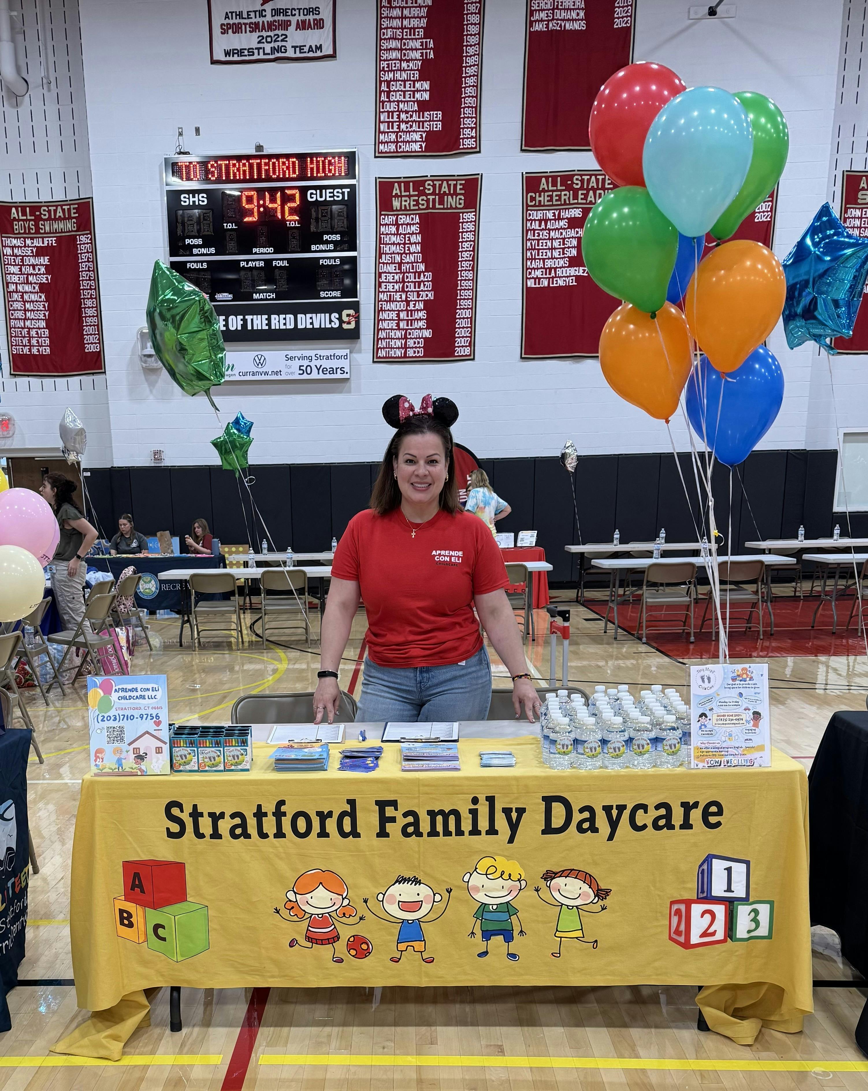 Person in Mickey Mouse ears standing behind a Stratford Family Daycare table