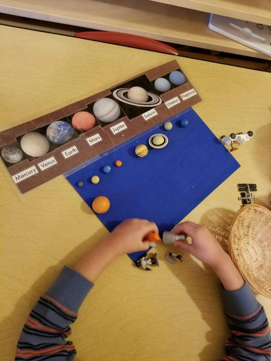 Child's hands arranging planet models on a blue mat next to a solar system display