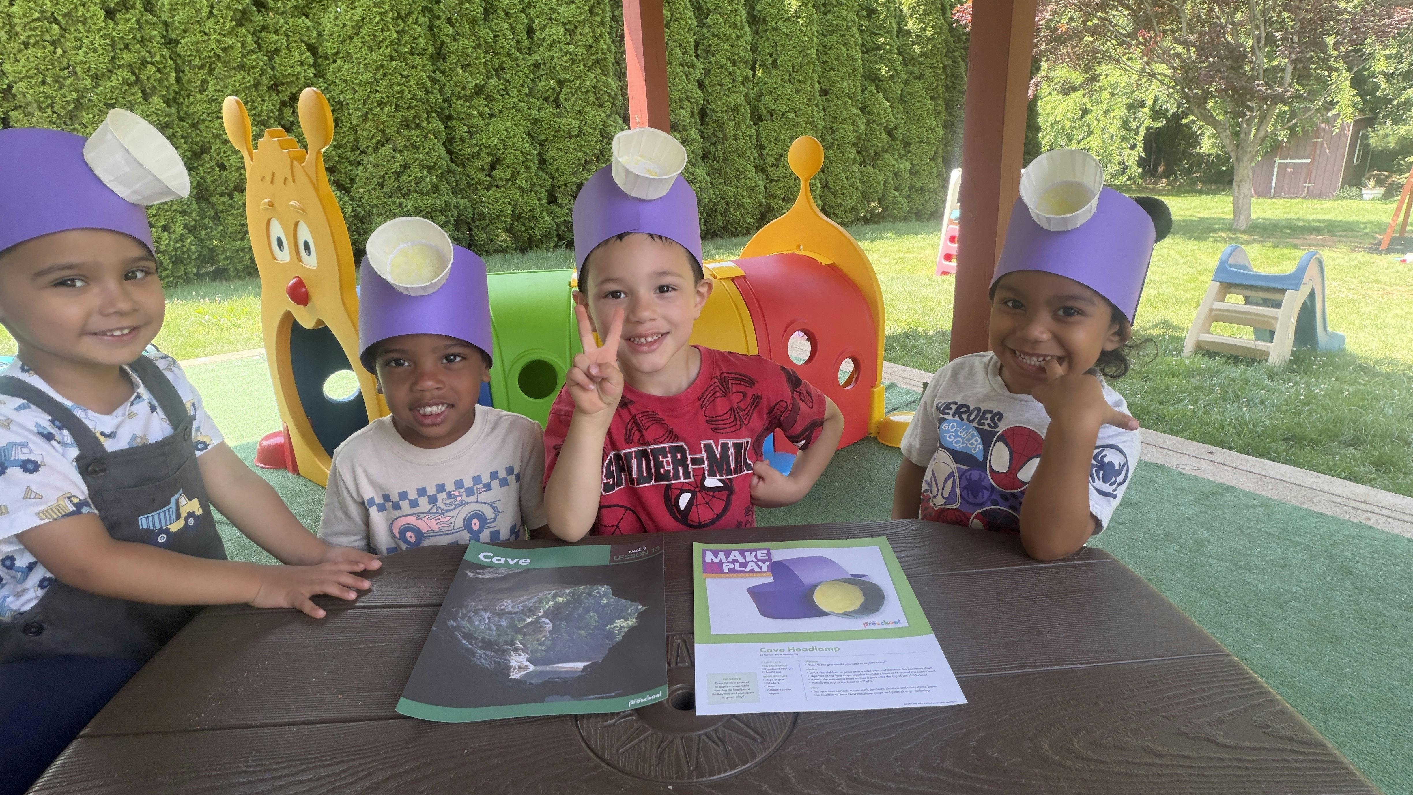 Four children sitting at a table outdoors wearing homemade paper headlamps