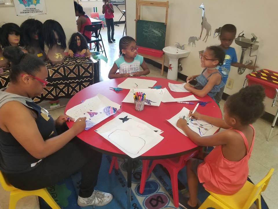 Adult and children drawing at a red table