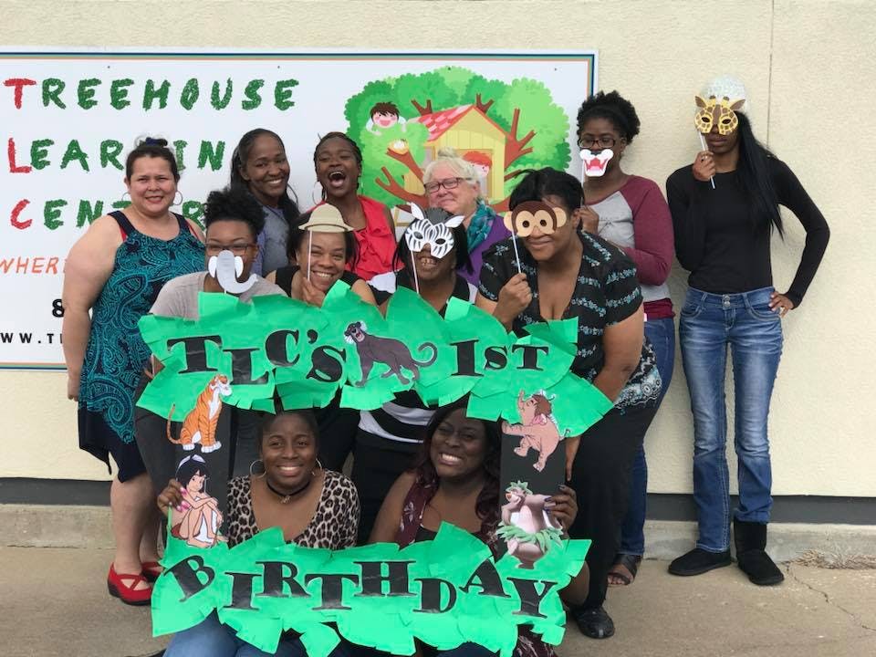 Group of people holding a sign that says "TLC's 1st Birthday"