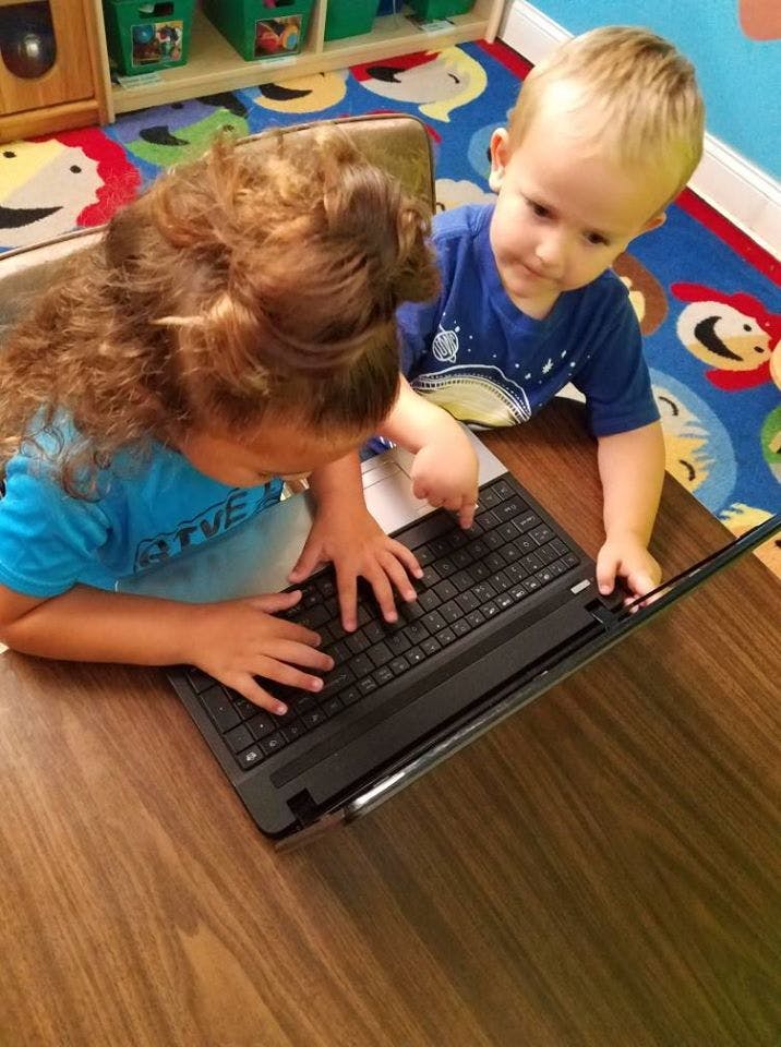 Two children typing on a laptop