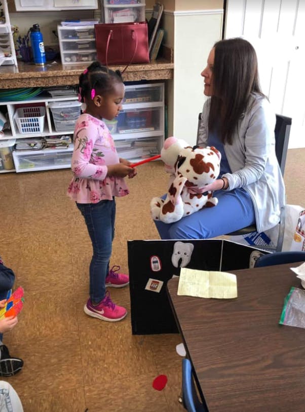 Child holding a red stick toward a stuffed animal held by an adult