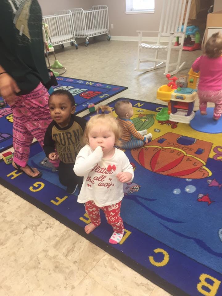 Three children on a colorful rug in a room with cribs