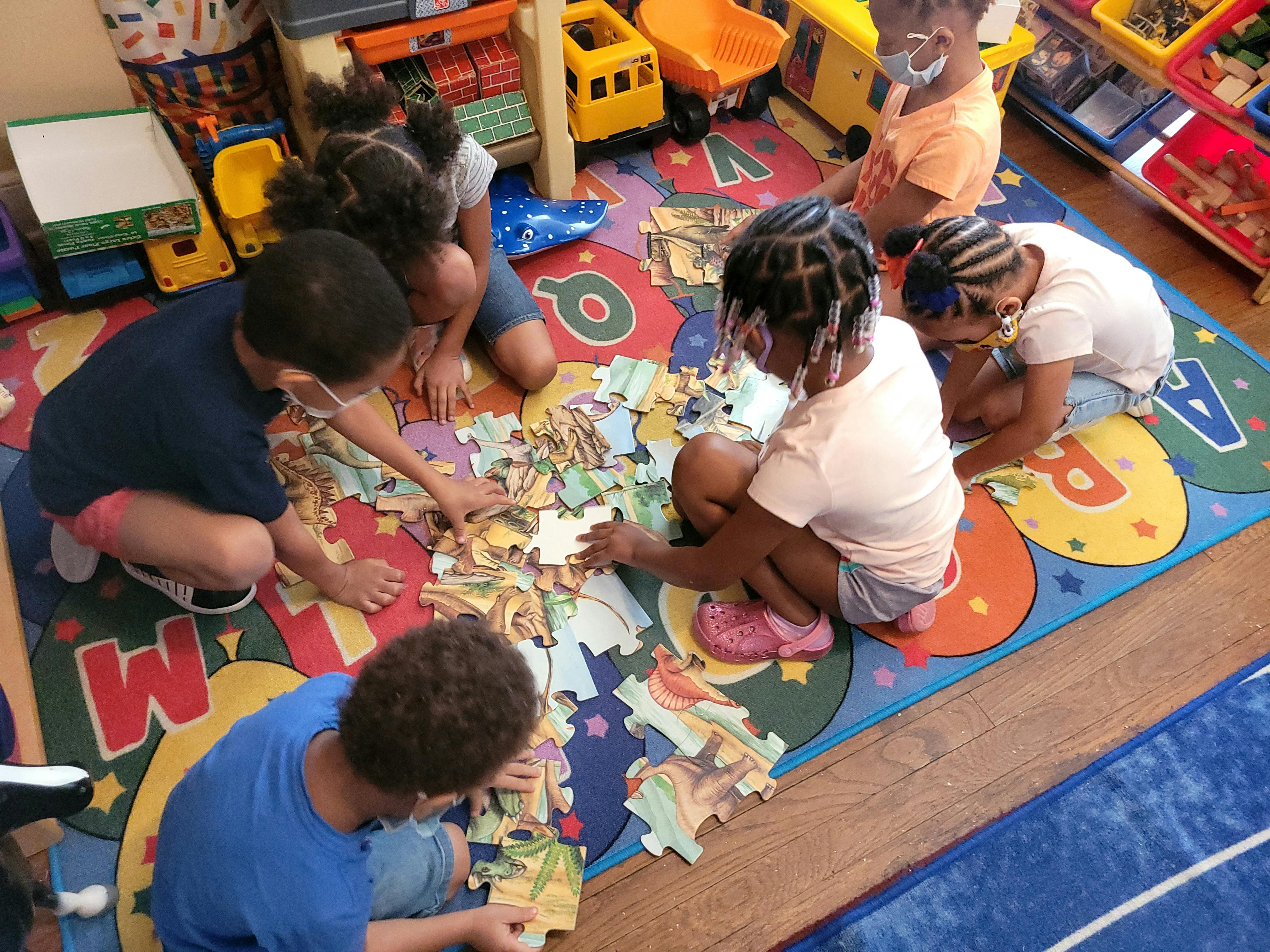 Children on a colorful rug assembling a large floor puzzle