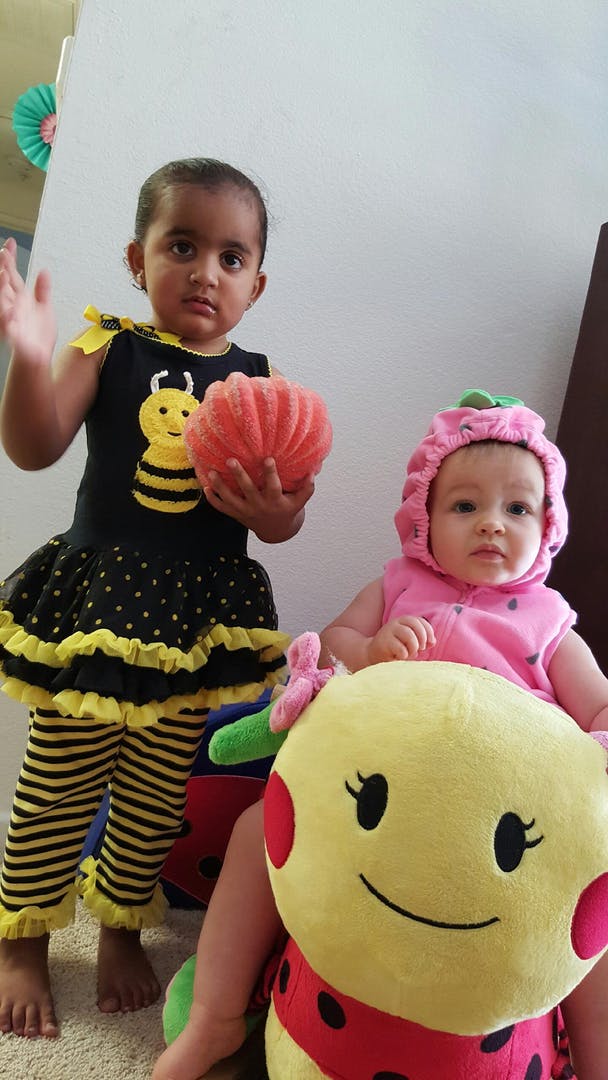 Child in bee costume holding a pumpkin next to a baby in a strawberry costume