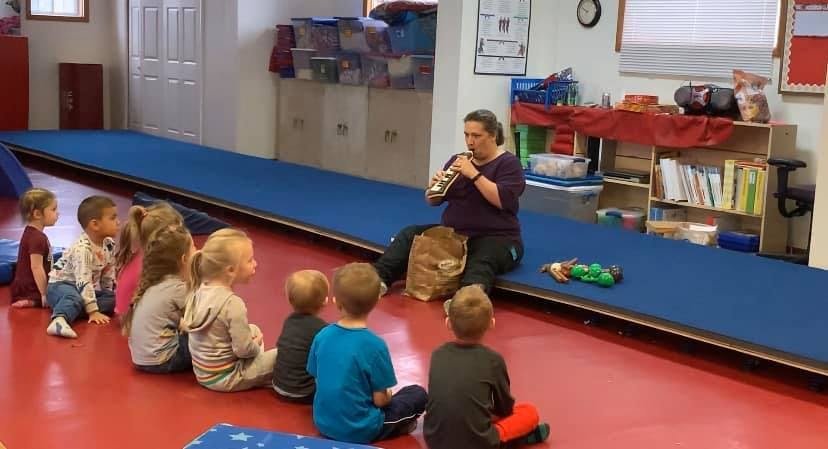 Adult reading to a group of children sitting on the floor in a classroom