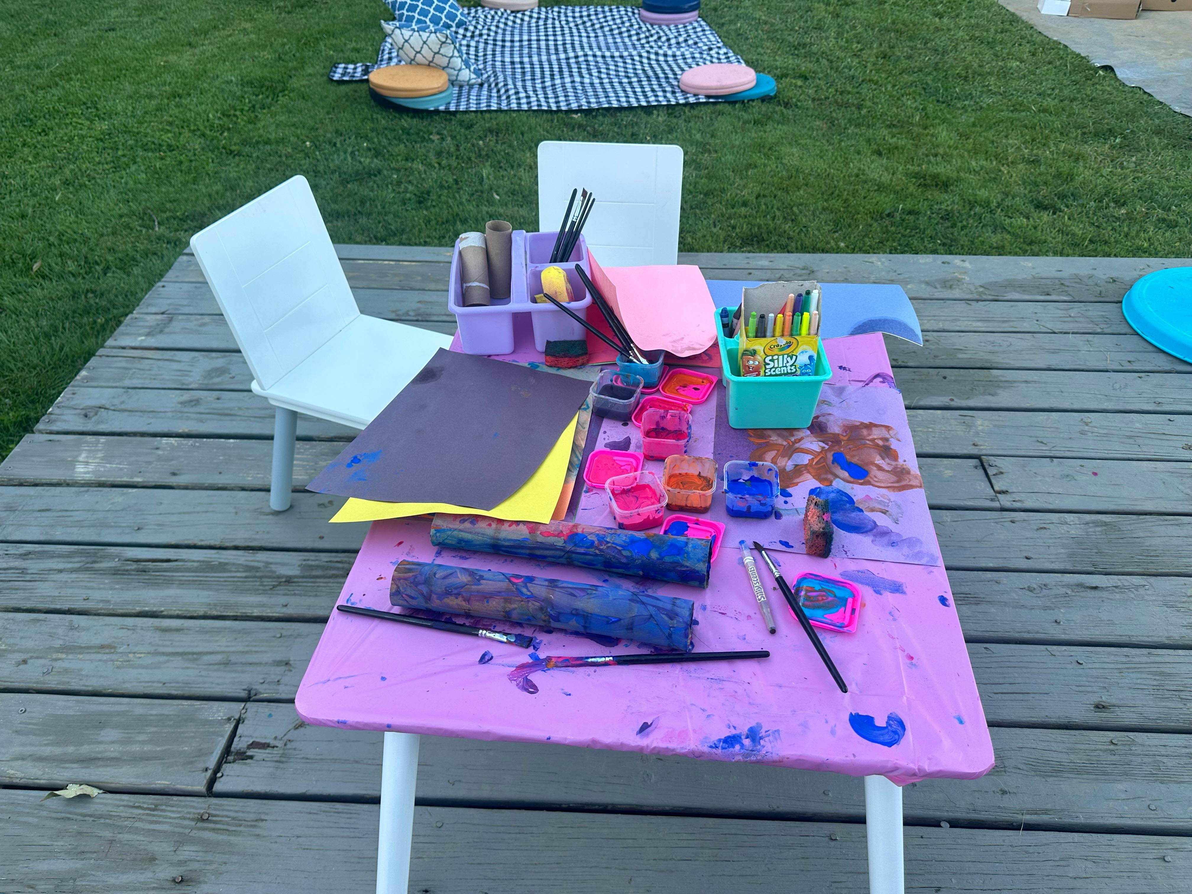 Art supplies on a purple table on a wooden deck