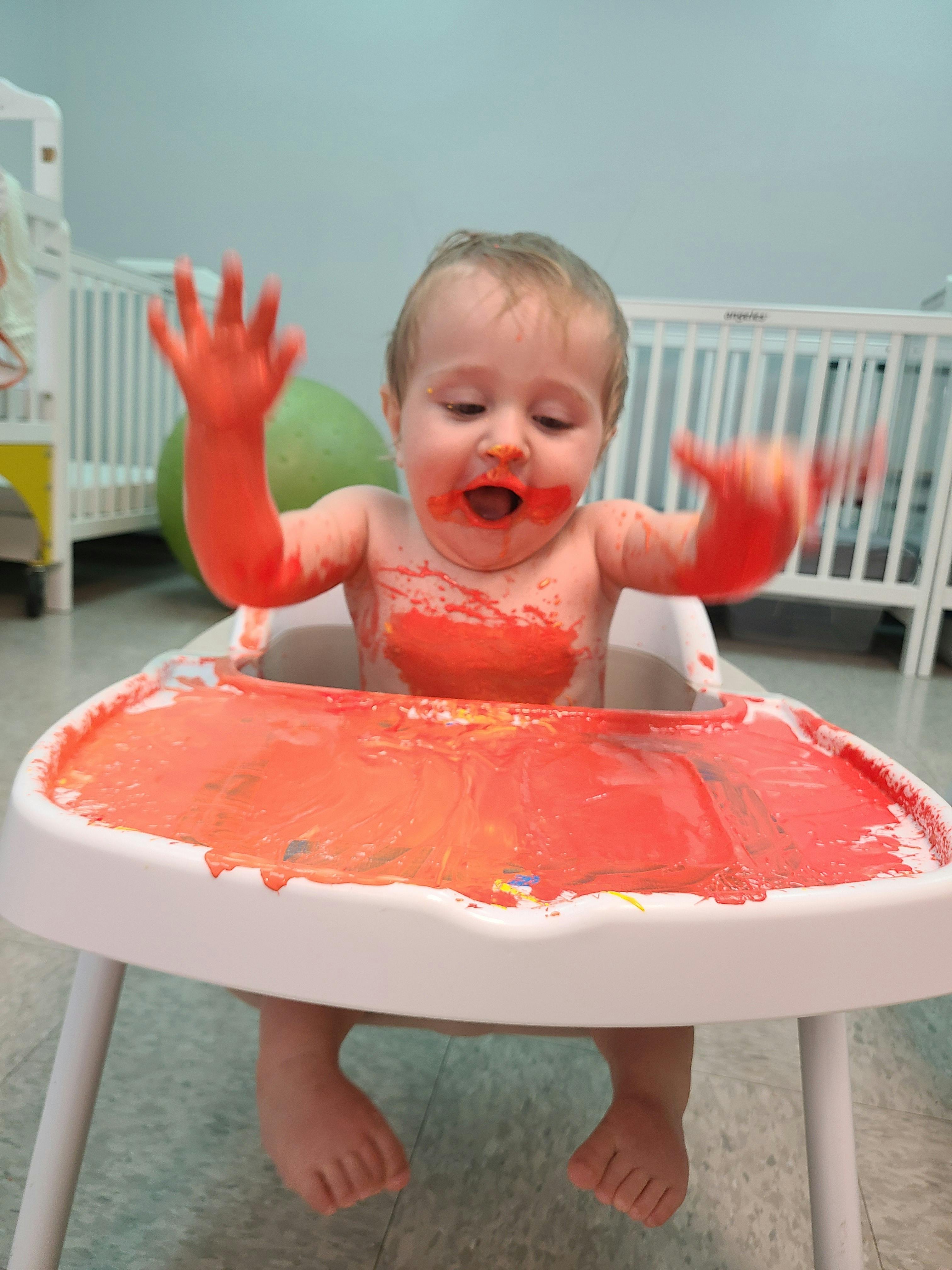 Child in a high chair covered in red paint