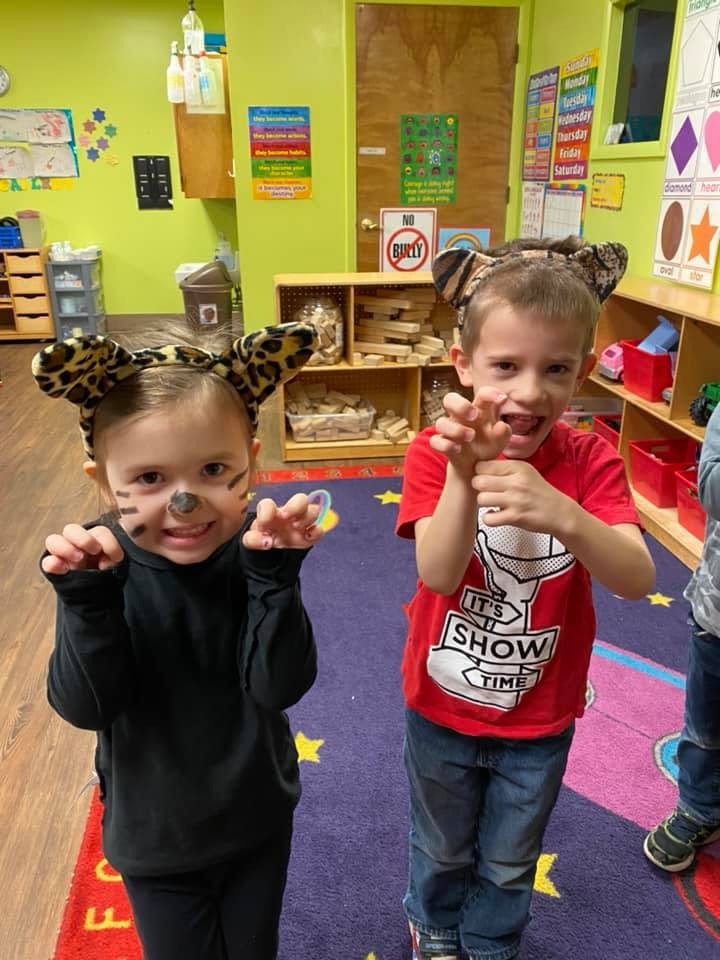 Two children in a classroom, one with face paint and leopard print ears