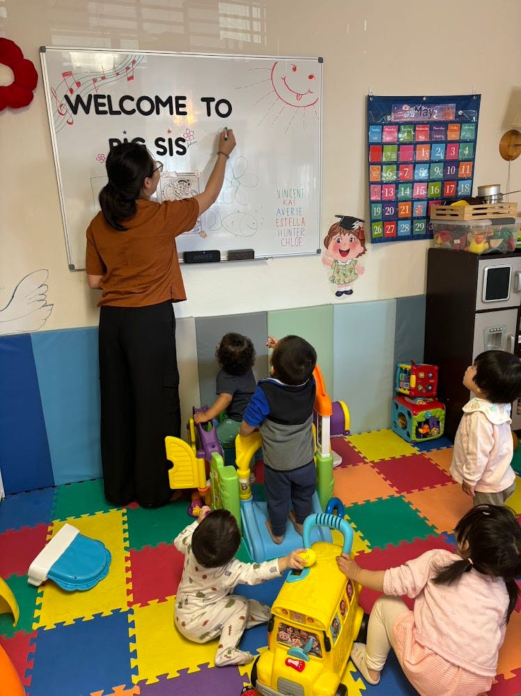 Person writing on a whiteboard with children playing on a colorful mat