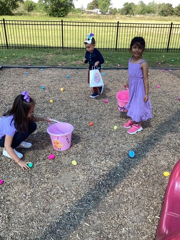 Three children collecting colorful eggs on wood chips