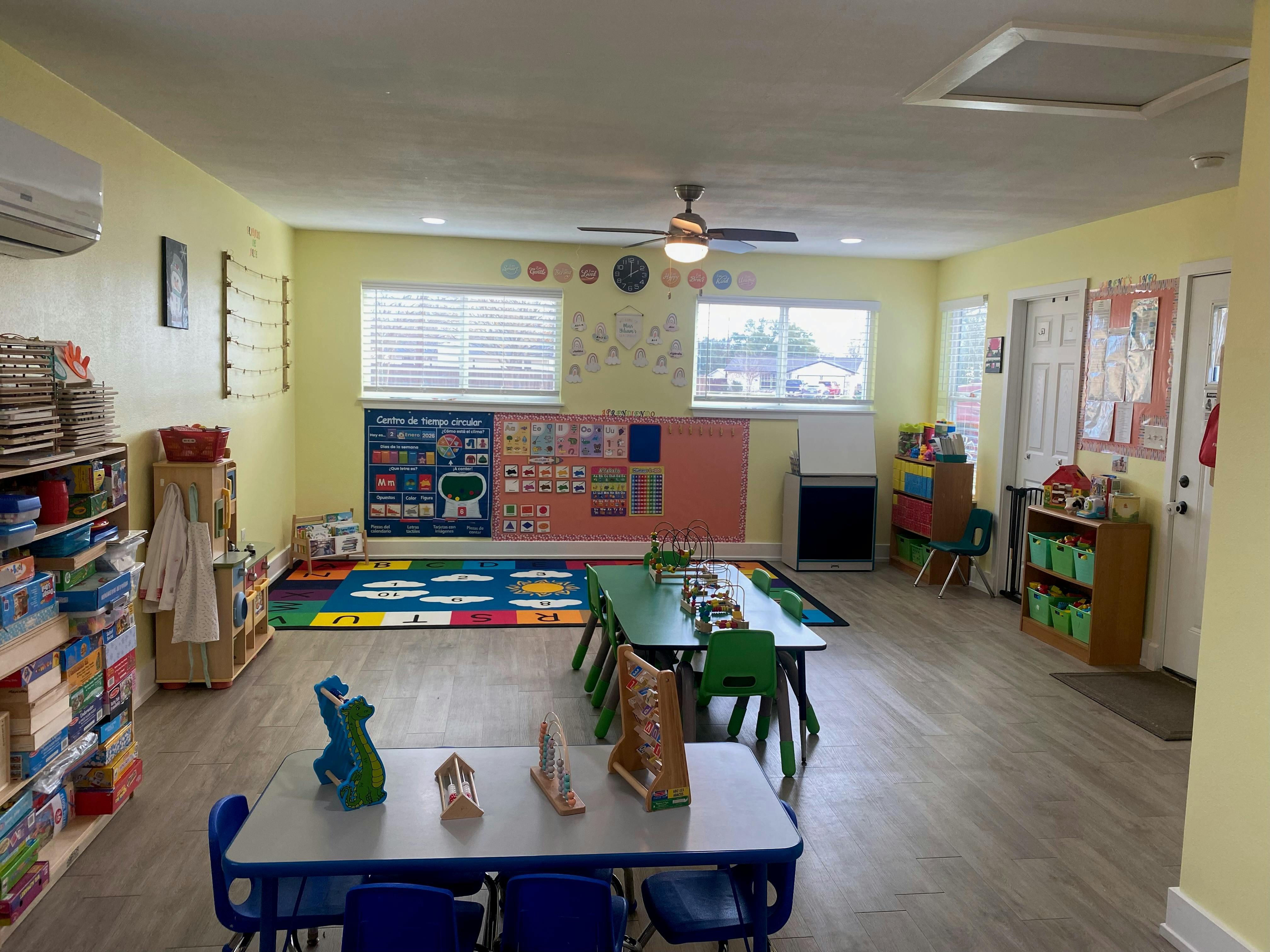 Classroom with tables, chairs, colorful rug, shelves, and educational posters